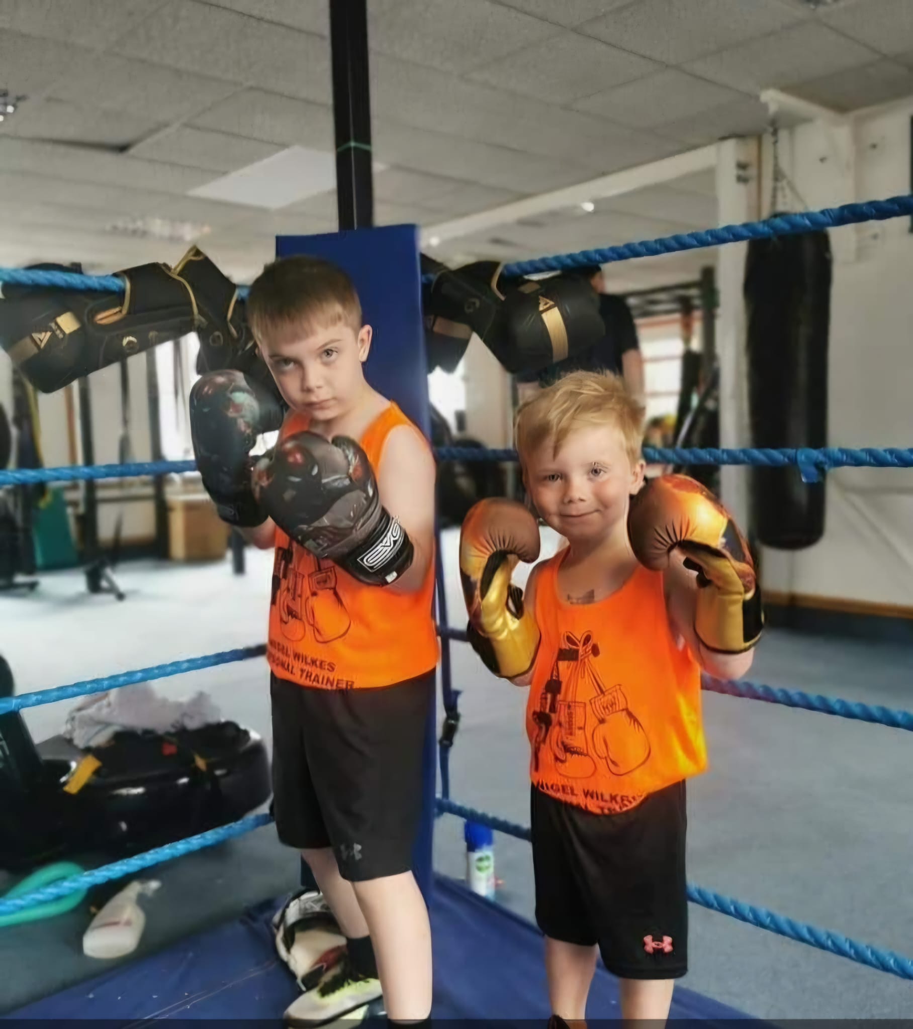 Two young boxers in orange Zestus vests with their fists up in the ring at Zestus Fitness.